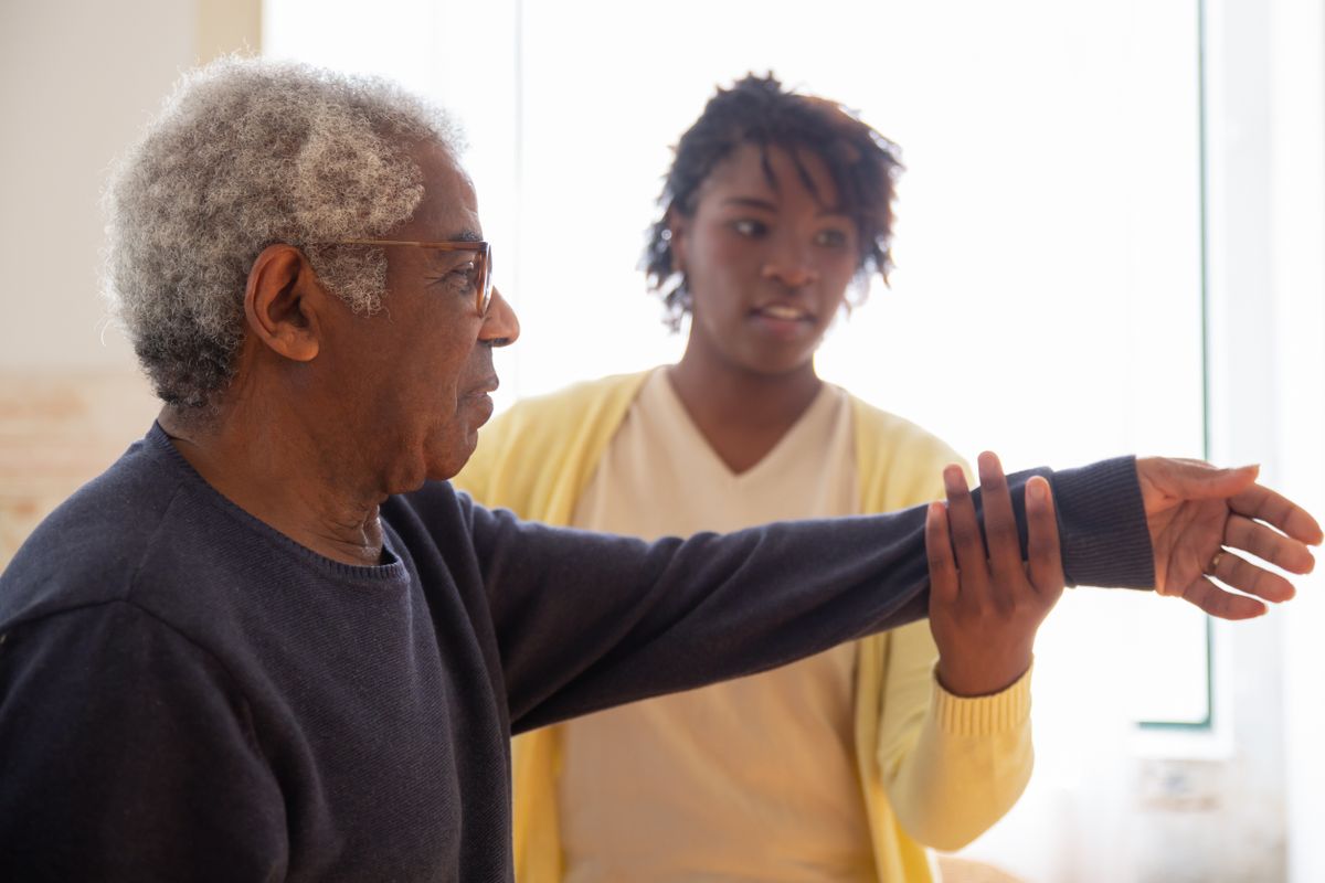 A companion guiding an older man through a gentle arm stretch
